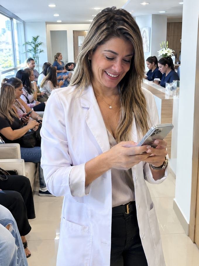 Médica sonriendo al ver en su celular la agenda llena, con la sala de espera ocupada